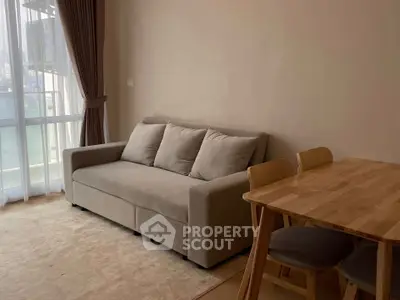 Cozy living room with modern sofa and dining table, featuring natural light from large window.