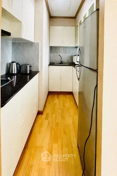 Modern kitchen with sleek appliances and wooden flooring, featuring a spacious fridge and ample storage cabinets.