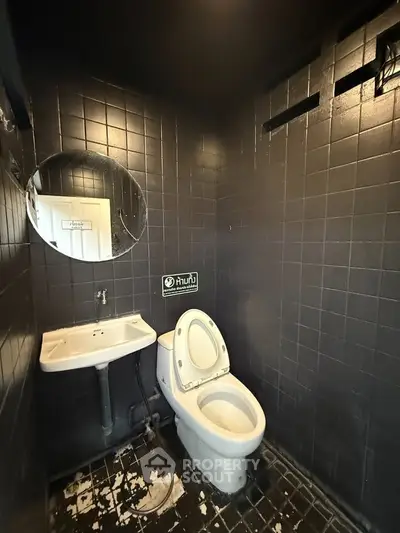 Modern black-tiled bathroom with round mirror and white fixtures.