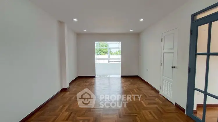 Spacious empty room with wooden flooring and large window view.