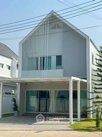 Modern two-story house with sleek design and large windows, featuring a spacious carport and minimalist landscaping.