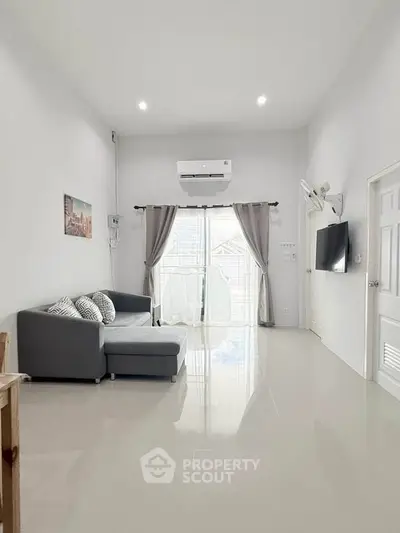 Spacious modern living room with sleek sofa and wall-mounted TV, featuring large windows for natural light.