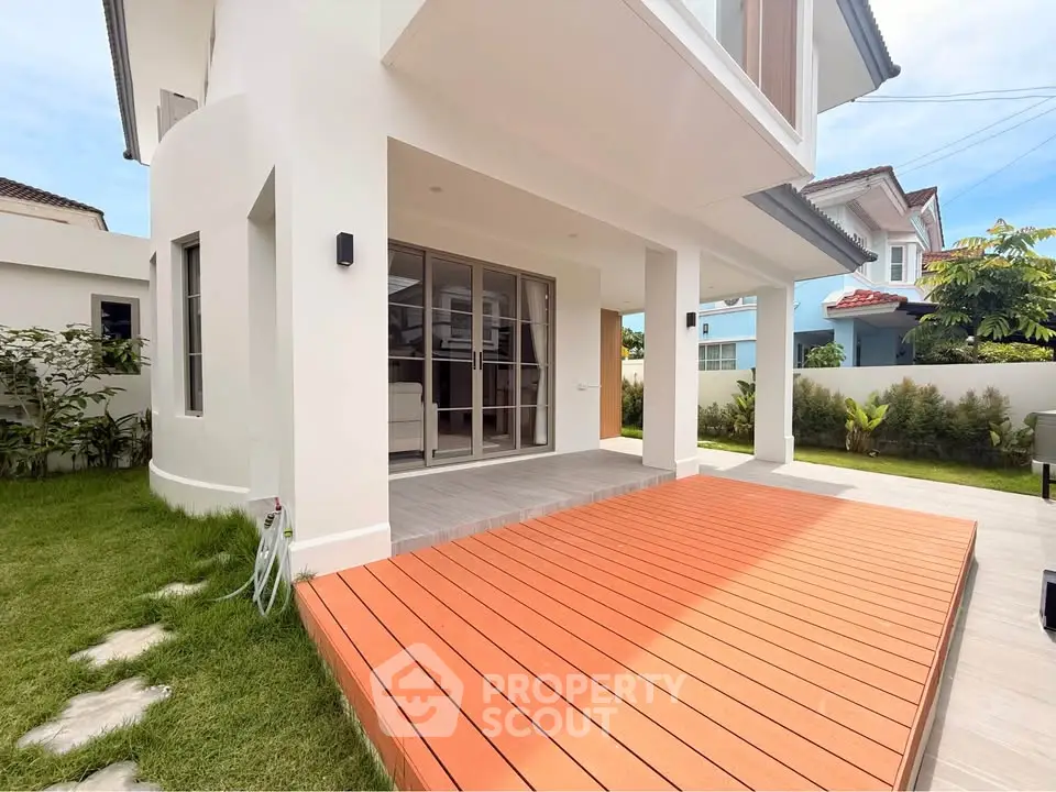 Modern two-story house with spacious wooden deck and lush green lawn, perfect for outdoor relaxation.