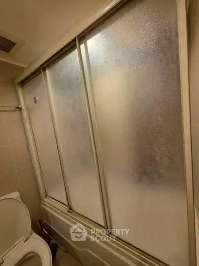 Compact bathroom with frosted glass shower doors and toilet, ideal for efficient space use.