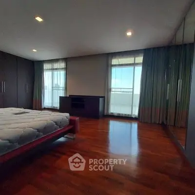 Spacious bedroom with wooden flooring and large windows offering natural light.