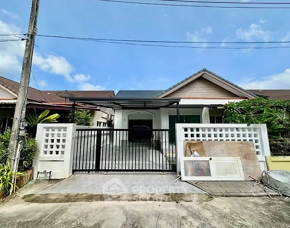 Charming single-story house with gated driveway and lush greenery, perfect for family living.