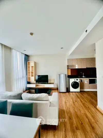Modern living room with open kitchen, featuring washing machine and sleek wooden flooring.