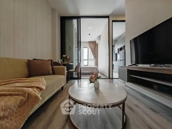 Modern living room with cozy sofa and large TV, open to bedroom and kitchen.