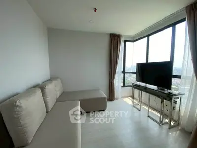 Modern living room with large windows and city view, featuring a sleek sofa and flat-screen TV.