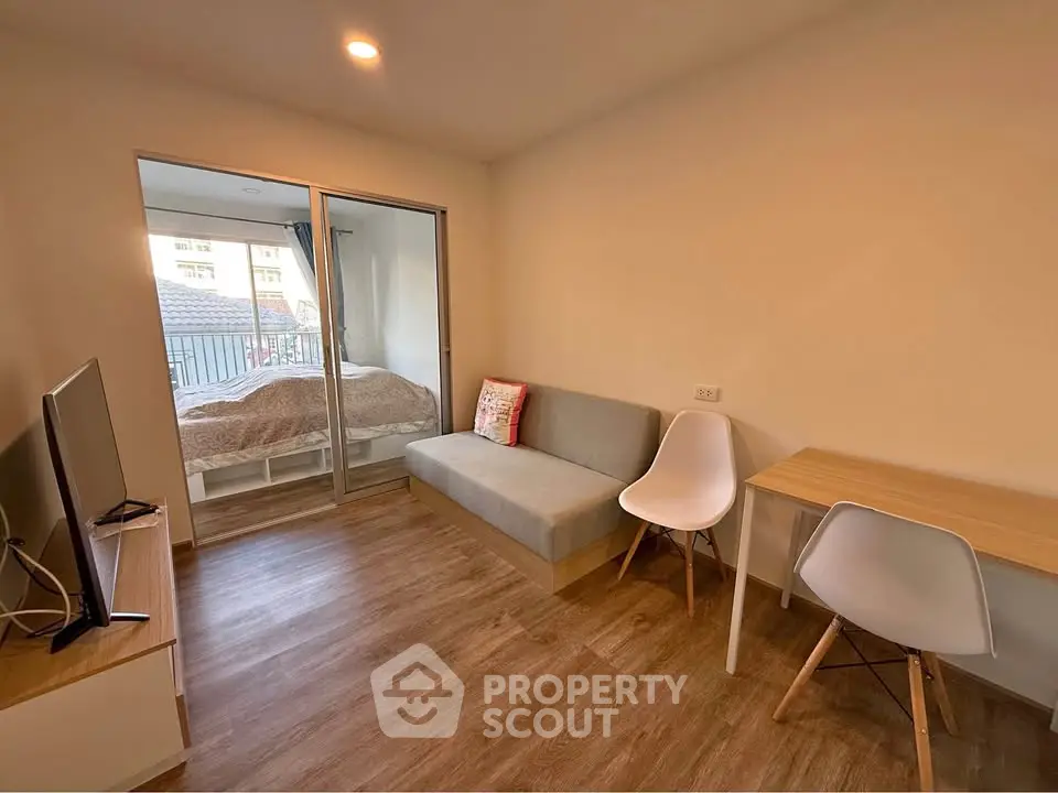 Modern studio apartment with cozy living area and bedroom, featuring sleek furniture and wooden flooring.