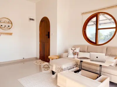 Charming living room with unique round window and cozy decor, perfect for relaxation and work-from-home setup.