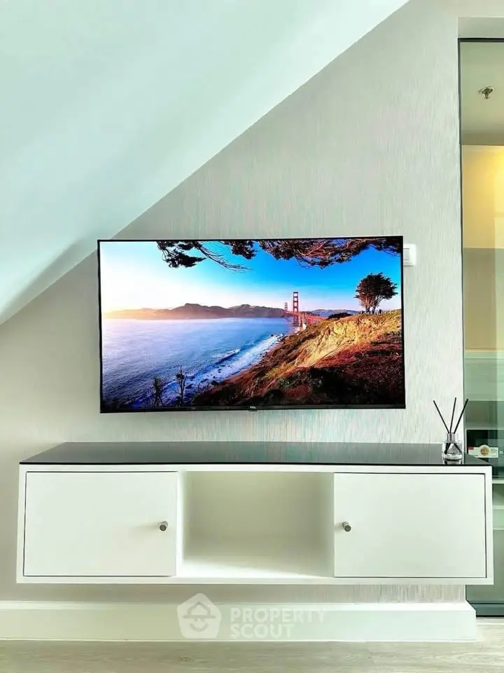 Modern living room with sleek TV setup and stylish cabinet under sloped ceiling.