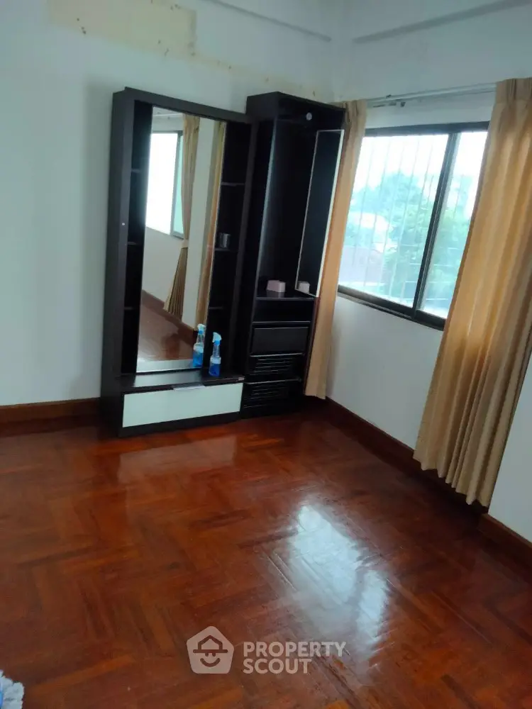 Spacious bedroom with wooden flooring and large window for natural light.
