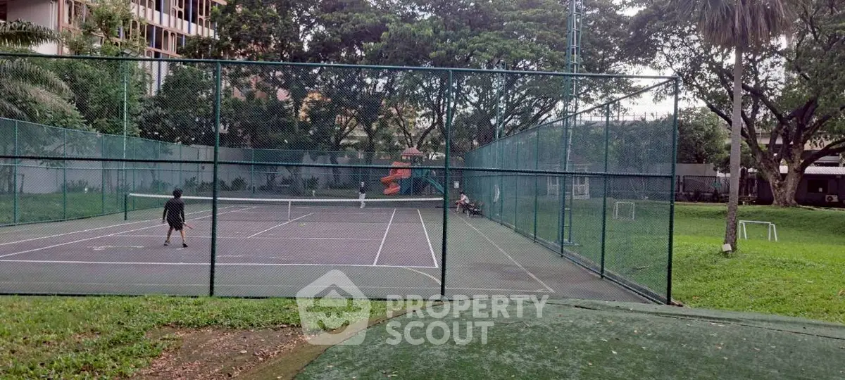 Spacious outdoor tennis court surrounded by lush greenery in a residential complex.