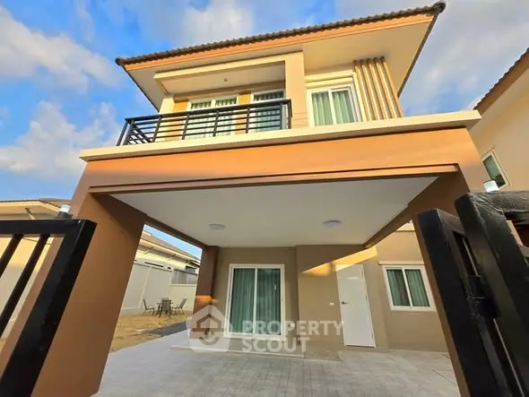 Modern two-story house with balcony and gated entrance under a clear blue sky.