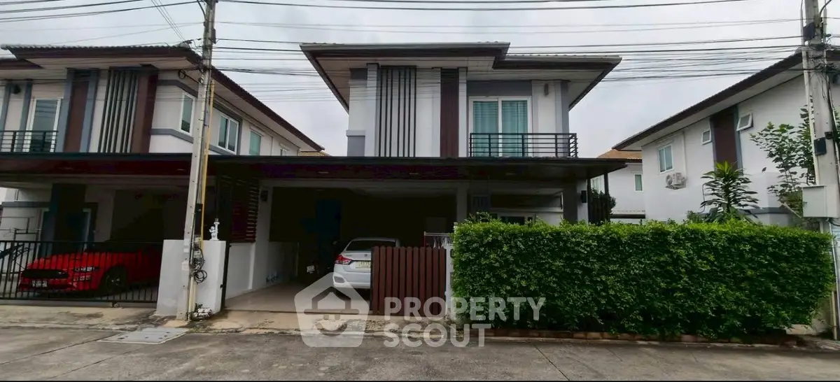 Modern two-story house with carport and lush greenery in suburban setting.