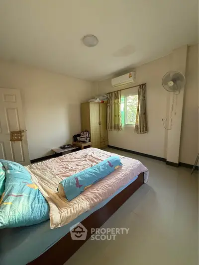 Cozy bedroom with natural light, featuring a bed, wardrobe, and air conditioning.