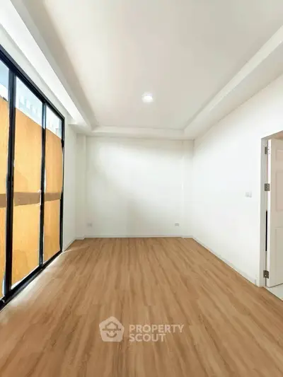 Spacious empty room with wooden flooring and large windows, perfect for customization.