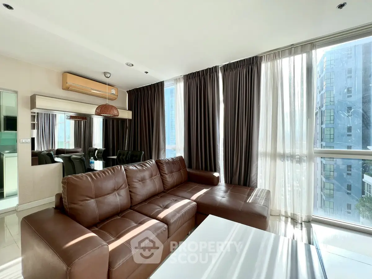 Spacious modern living room with large windows and brown leather sofa in a high-rise apartment.