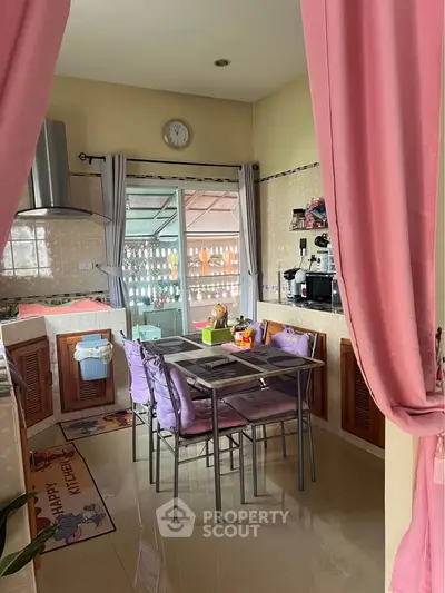 Charming kitchen with open layout and cozy dining area, featuring pink curtains and modern appliances.