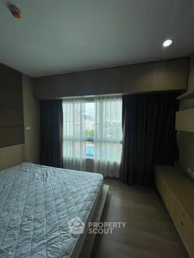 Spacious bedroom with large window and modern furnishings, offering ample natural light and city views.