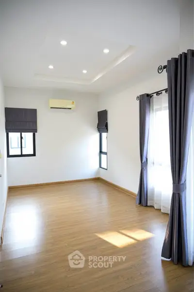 Spacious empty room with wooden flooring and large windows, perfect for customization.