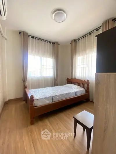Bright bedroom with wooden flooring and elegant curtains, featuring a classic wooden bed and natural light.