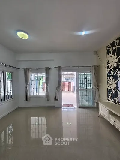 Spacious living room with large windows and elegant curtains, featuring glossy tiled floors and modern lighting.