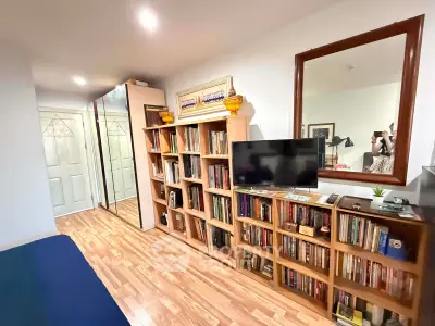 Cozy study room with wooden flooring, large mirror, and extensive bookshelf collection.