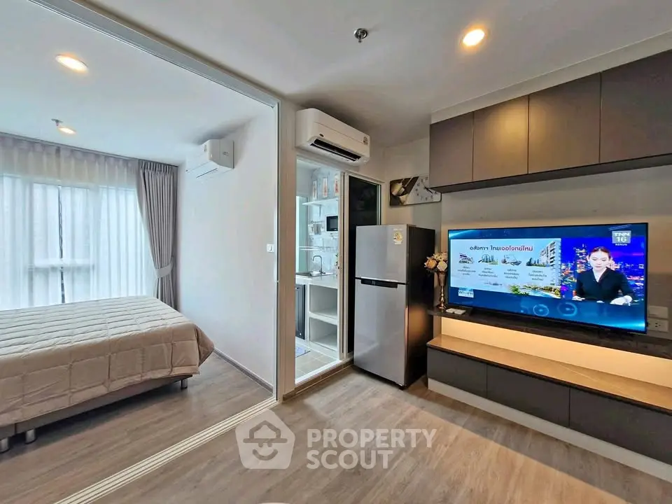 Modern apartment interior with open living room and bedroom, featuring sleek furniture and a large TV.