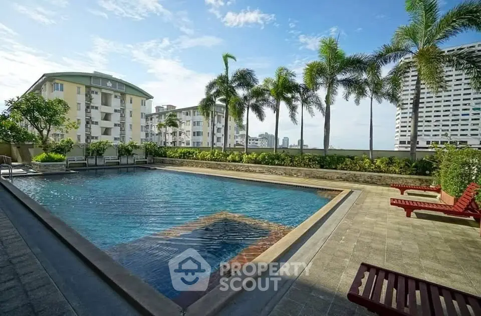 Luxurious condominium pool area with palm trees and city view, perfect for relaxation and leisure.