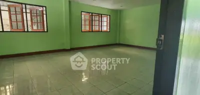 Spacious empty room with green walls and tiled floor, featuring large windows for natural light.