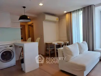 Modern open-plan living room with kitchen and dining area, featuring a washing machine and sleek furniture.
