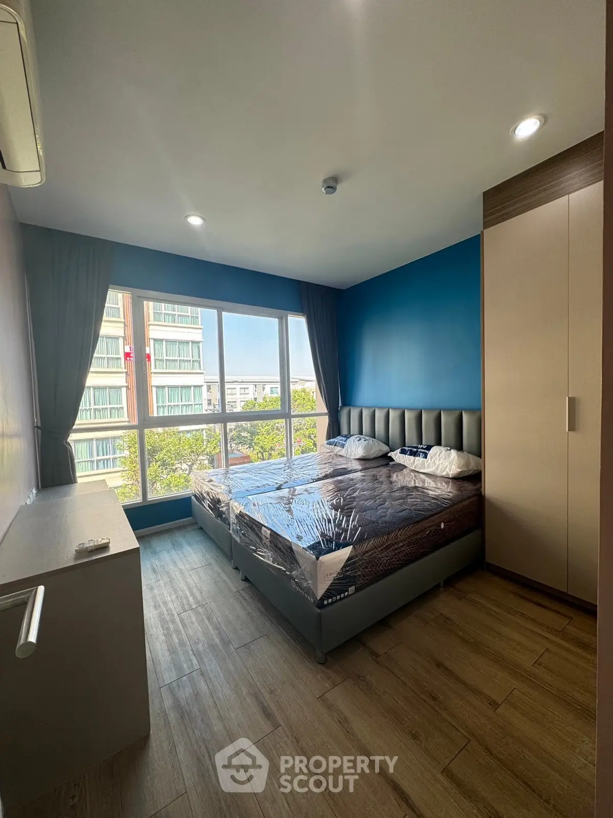 Modern bedroom with large window and blue accent wall in a high-rise apartment