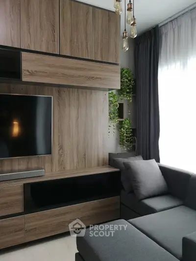 Modern living room with sleek wooden cabinetry and cozy gray sofa, featuring stylish lighting and lush greenery.