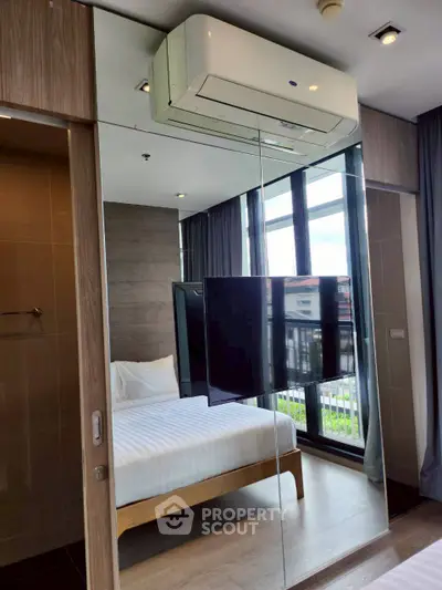 Modern bedroom with mirrored wall, air conditioning, and large windows for natural light.