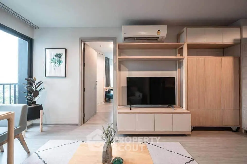 Modern living room with stylish furniture and large TV, featuring a sleek air conditioner and natural light.