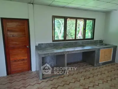 Spacious kitchen with concrete countertops and large window overlooking greenery.