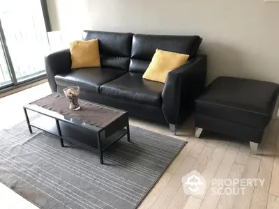 Elegant living room with a luxurious black leather sofa complemented by vibrant yellow cushions, a chic coffee table, and a stylish gray area rug.