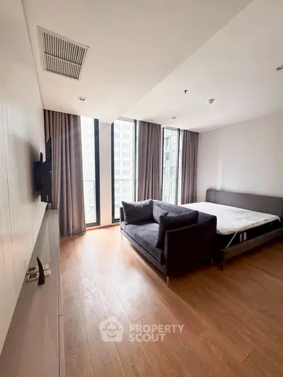 Modern bedroom with large windows and wooden flooring in a high-rise apartment.
