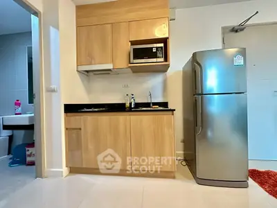 Modern compact kitchen with wooden cabinets and stainless steel fridge in cozy apartment.