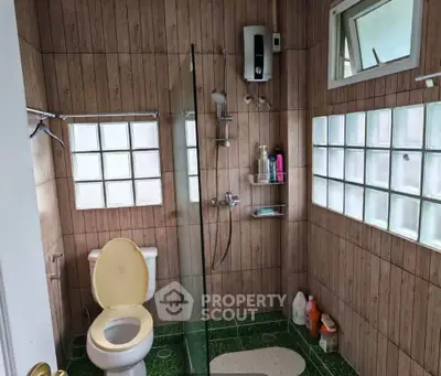 Charming bathroom with glass shower and wooden panel walls, featuring modern fixtures and natural light.