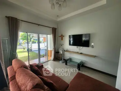 Spacious living room with modern decor and garden view, featuring a wall-mounted TV and comfortable seating.