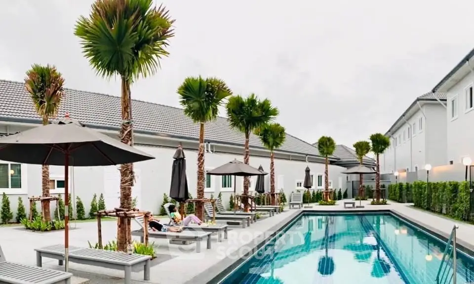Luxurious outdoor pool area with palm trees and sun loungers in modern residential complex.