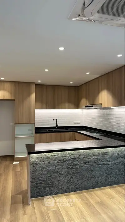 Modern kitchen with sleek black countertops and wooden cabinetry, featuring recessed lighting and a stylish open layout.