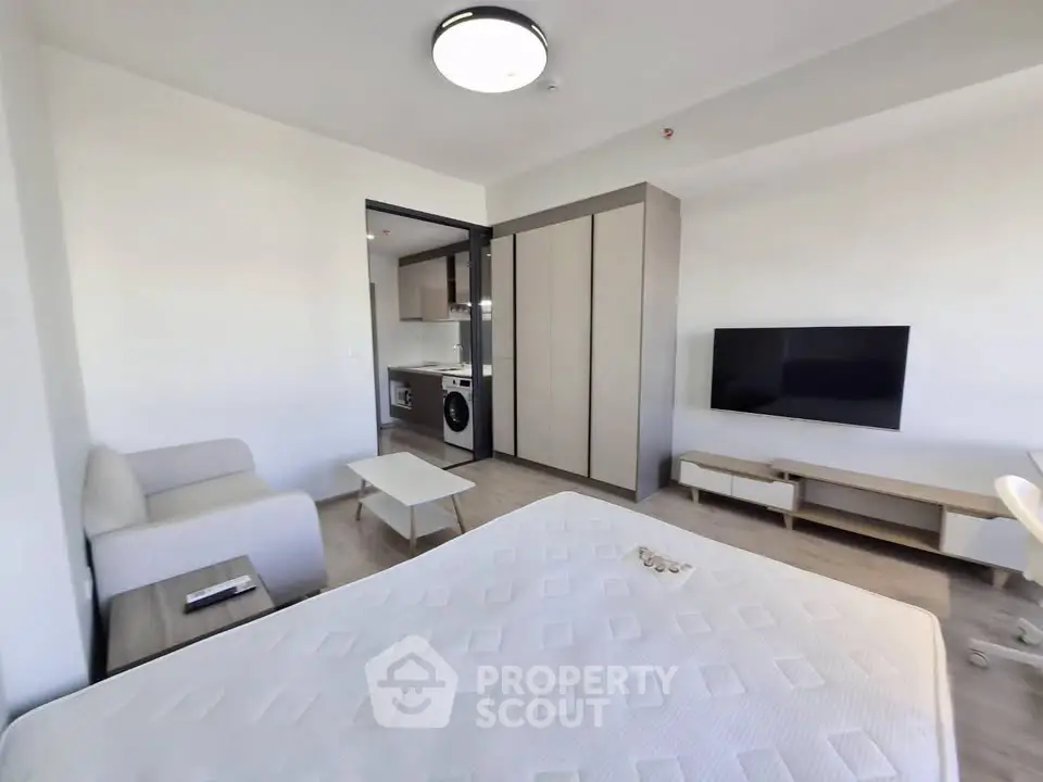 Modern studio apartment with open layout, featuring a cozy living area and sleek kitchen appliances.