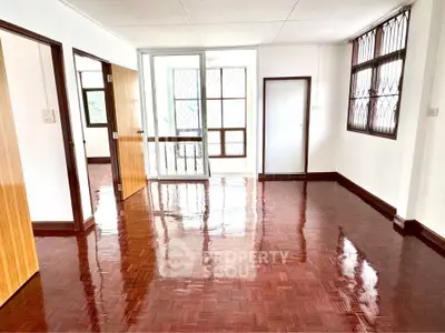 Spacious living room with glossy wooden floors and large windows for natural light.