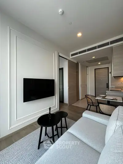 Modern living room with sleek design, featuring a wall-mounted TV, cozy sofa, and stylish kitchen area.