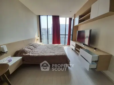 Modern bedroom with large windows and city view, featuring sleek furniture and a mounted TV.