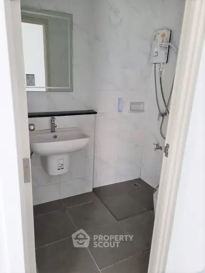 Modern bathroom with sleek design, featuring a wall-mounted sink and electric shower heater.